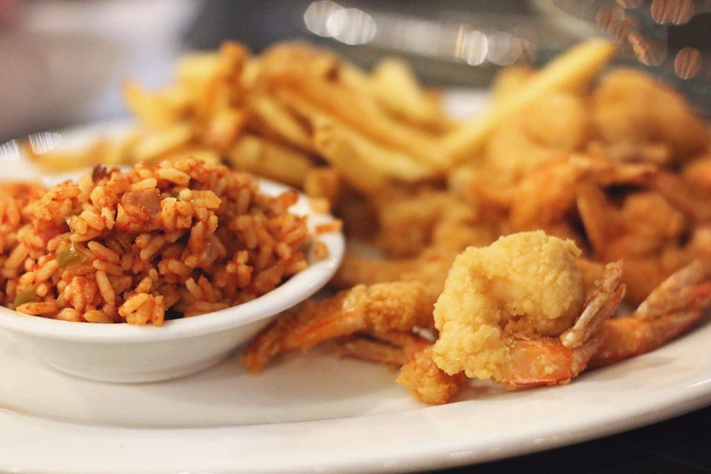 A plate of golden fried shrimp with a side of red beans and rice and fries in the background at Erica Davis Lowcountry in Savannah
