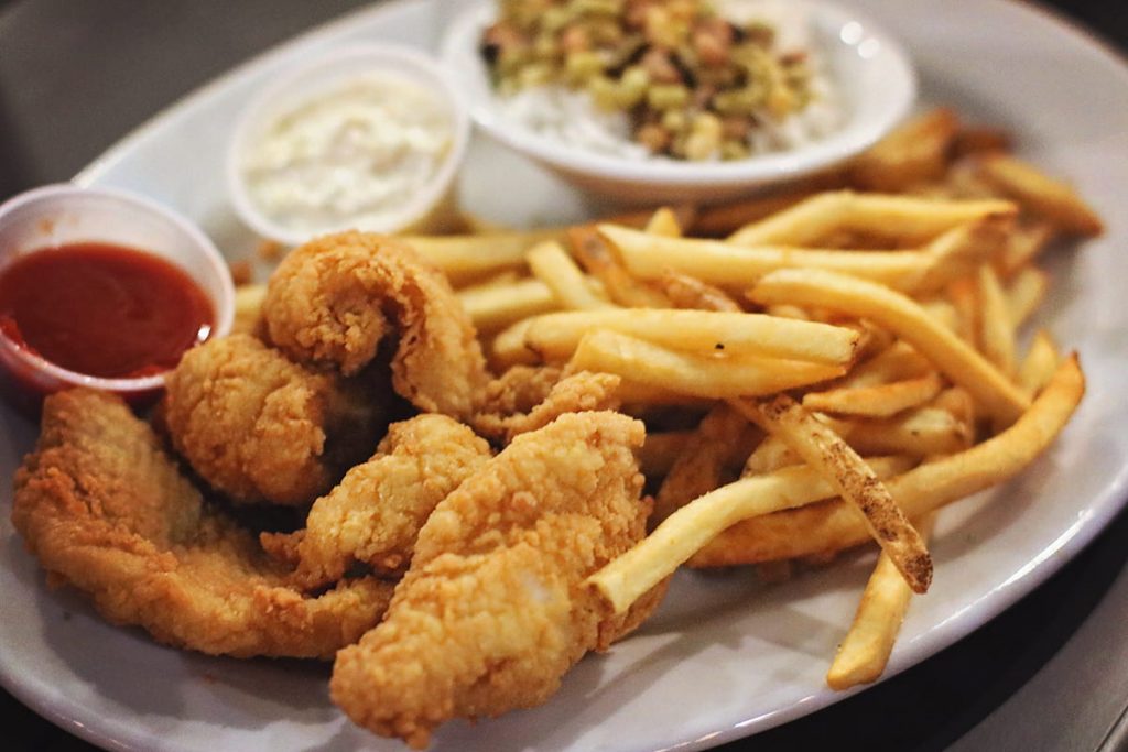 A plate of golden crispy fried flounder with fries, tartar sauce, and red seafood sauce