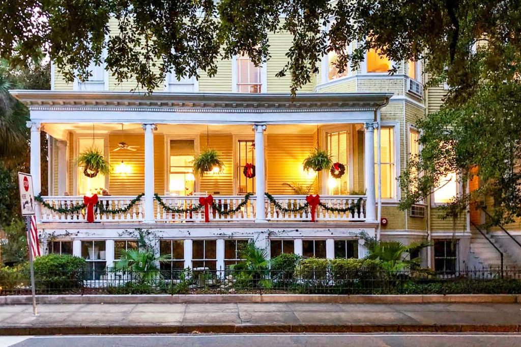 Cheery yellow B&B in Savannah with a white porch decorated in Christmas greenery and ribbons