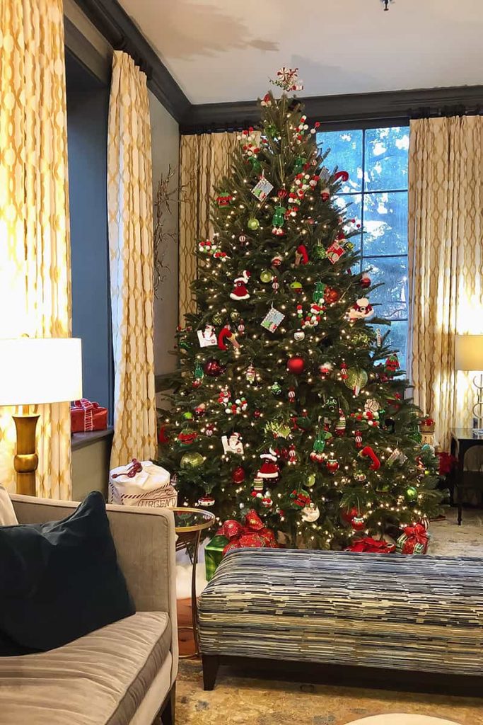 A traditional red and green Christmas tree in the reception area of East Bay Inn, with walls painted dark blue, gold-trimmed curtains, and warm lighting throughout
