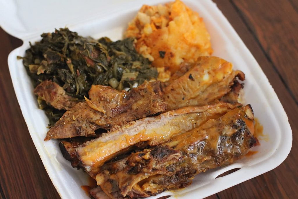 Styrofoam container from Munchies BBQ in Savannah with a hearty serving of ribs, collards, and golden mac n' cheese