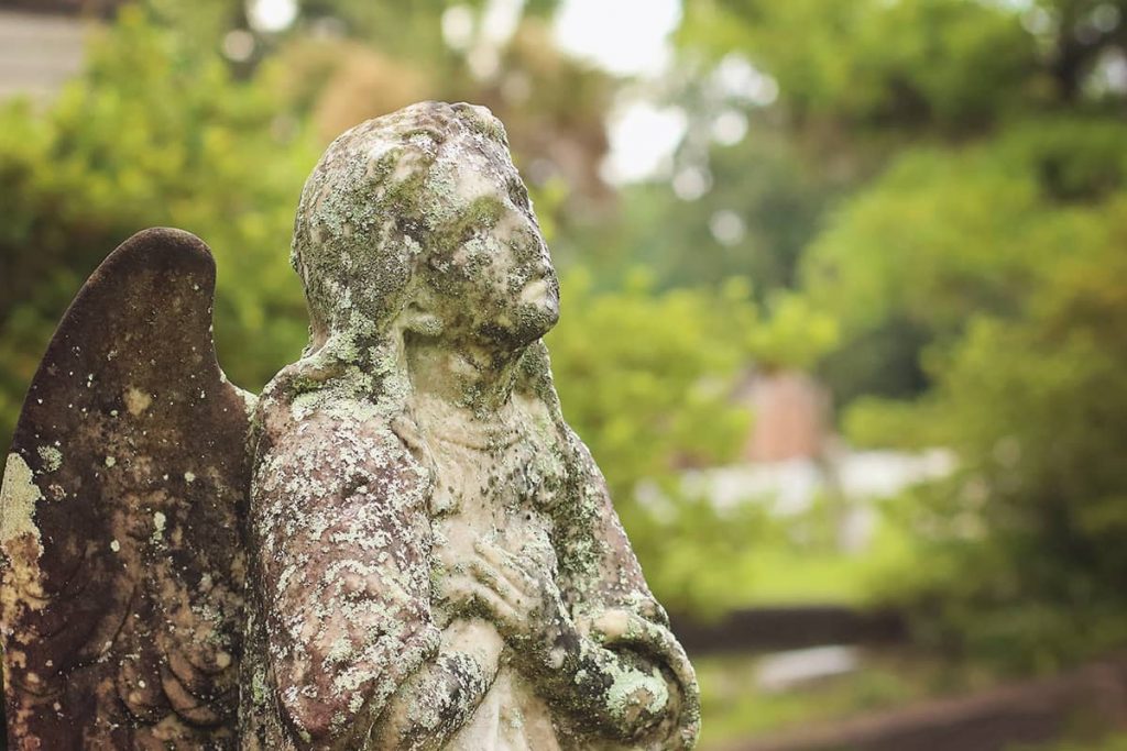 Close-up of an angel statue in Laurel Grove Cemetery North with arms crossed across its chest and lichens growing all over the statue