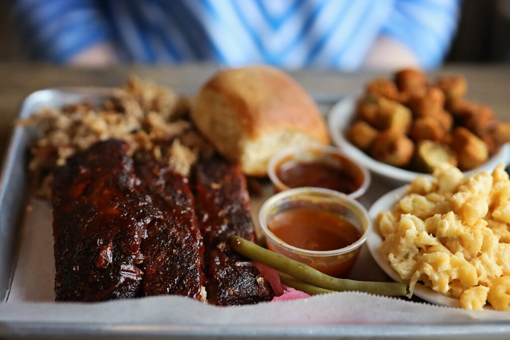 Combo BBQ plate at Erica Davis Lowcountry in Savannah filled with ribs, pulled pork, mac n' cheese, fried okra, two types of BBQ sauce, and a lightly-browned roll