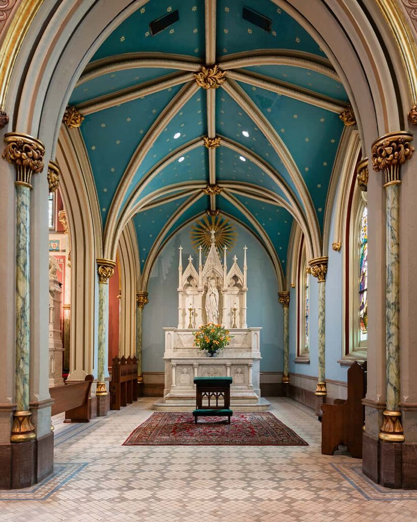 The tabernacle area in the Sacred Heart Chapel section of the Cathedral of St. John the Baptist. A white alter fills the back wall, which is painted pale blue with an arched, darker blue ceiling above