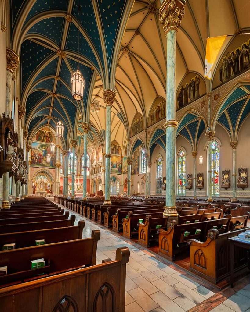 Interior of the Cathedral of St. John the Baptist with arched ceilings painted blue with gold accents. At least three rows of approximately 20 pews each fill the sanctuary