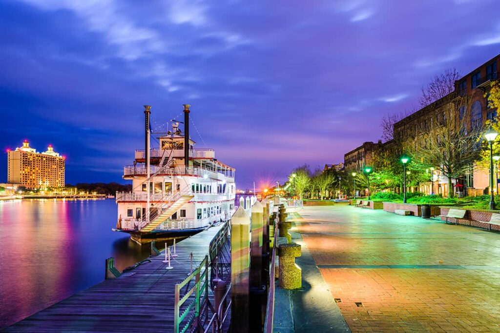 The Georgia Queen Steamboat docked along River Street in Savannah, Georgia with a purple-toned sunset in the background