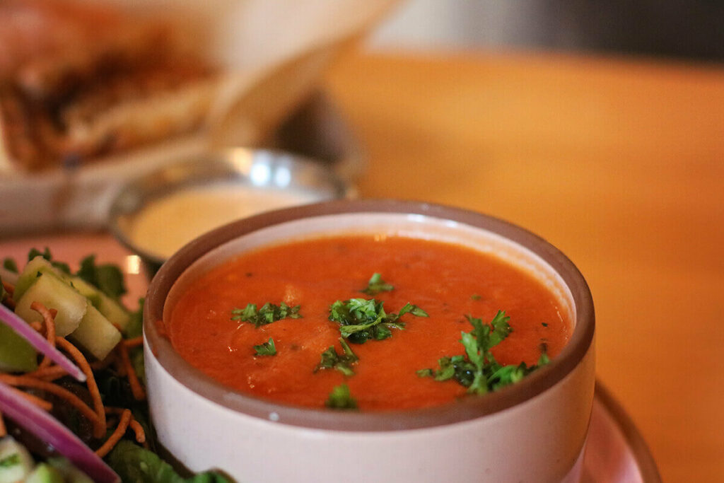 Close-up of a cup of tomato Thai soup topped with green spices