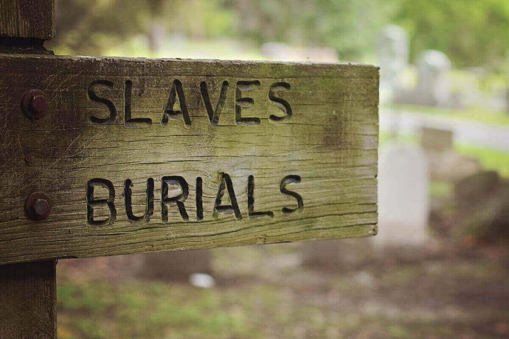 A simple old wooden sign at Laurel Grove South with rusted attachments and the words Slaves Burials etched into its face