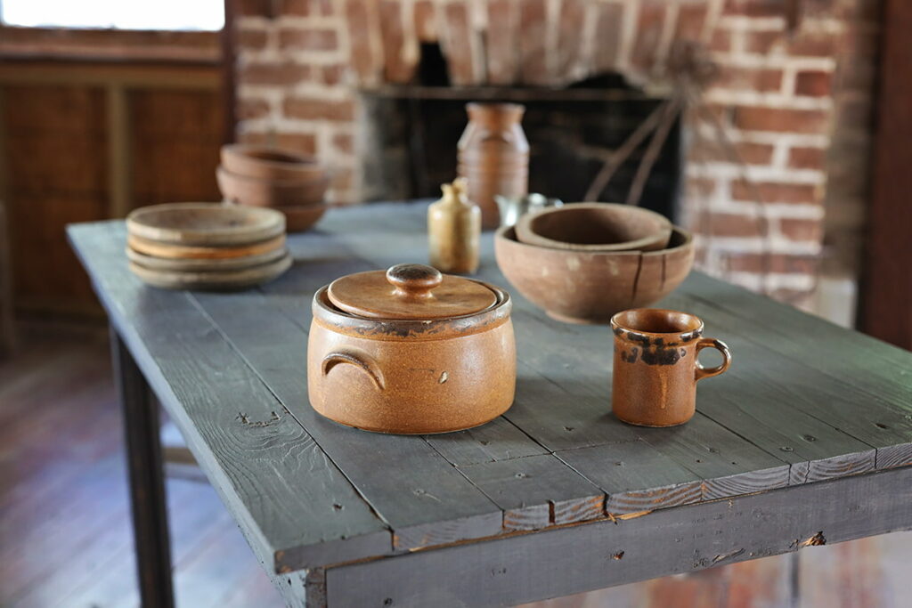 A simple grey-stained wooden tabletop with earthen-colored pottery in the carriage house of the Sorrel Weed House