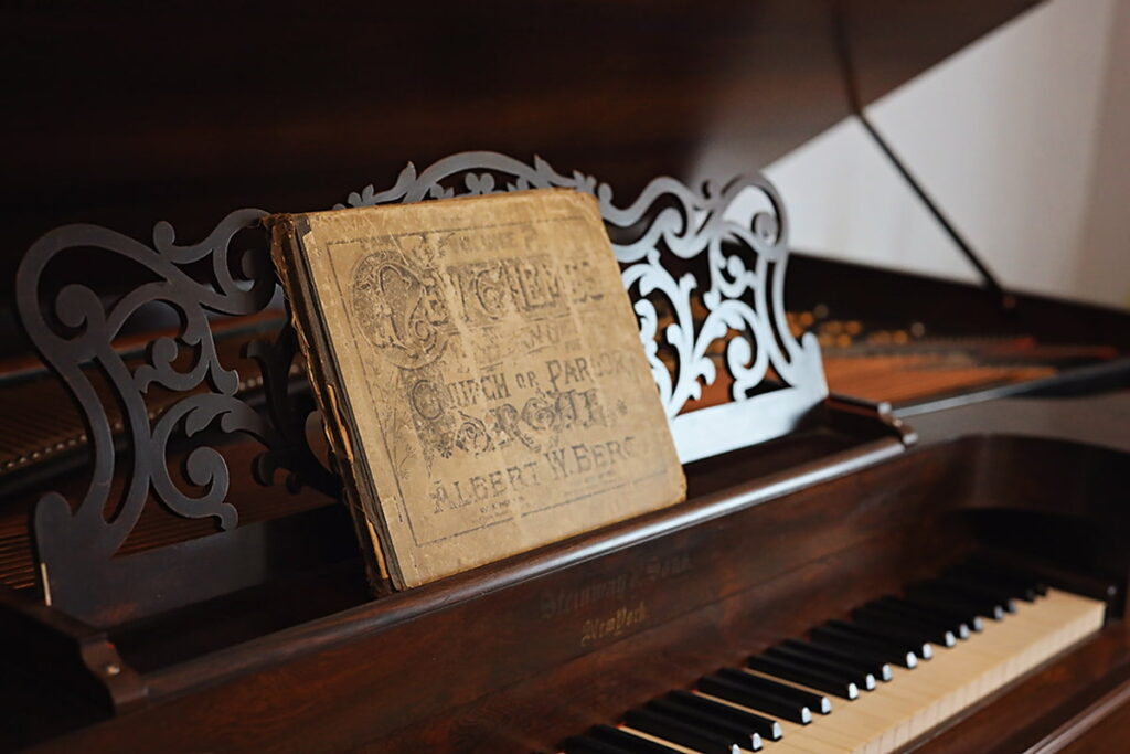 Antique sheet music pages rest against an intricate wooden scrolled backdrop on the historic Steinway square piano inside the Sorrel Weed House