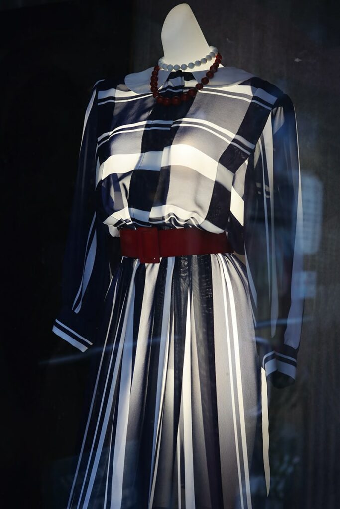 Window display of a vintage long-sleeved B&W dress with a burgundy belt displayed on a mannequin