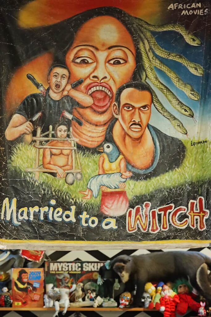 An African Movies poster hangs inside Graveface Records with images of a woman who has snakes for hair, a man with knives sticking out of his body, and another woman with a bird head. The movie title reads "Married to a Witch"