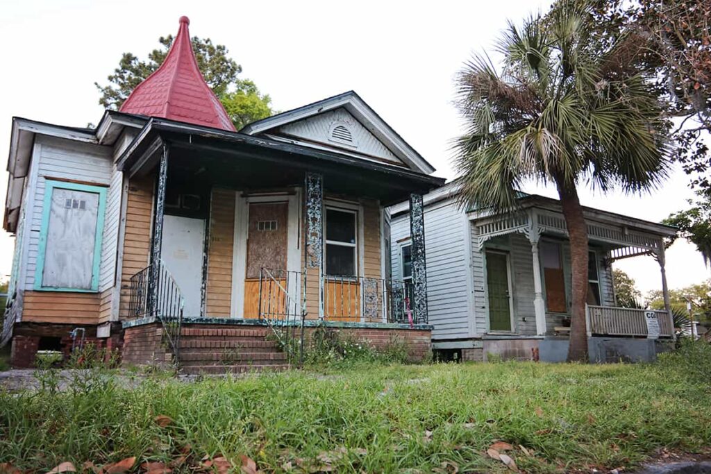 Low angle of two dilapidated homes in the Starland District with boards covering the windows and doors. The grass is overgrown