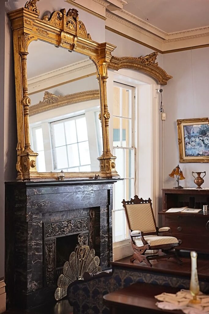 An oversized ornate gilded mirror rests atop a black marble fireplace in the ladies parlor of the Sorrel Weed House
