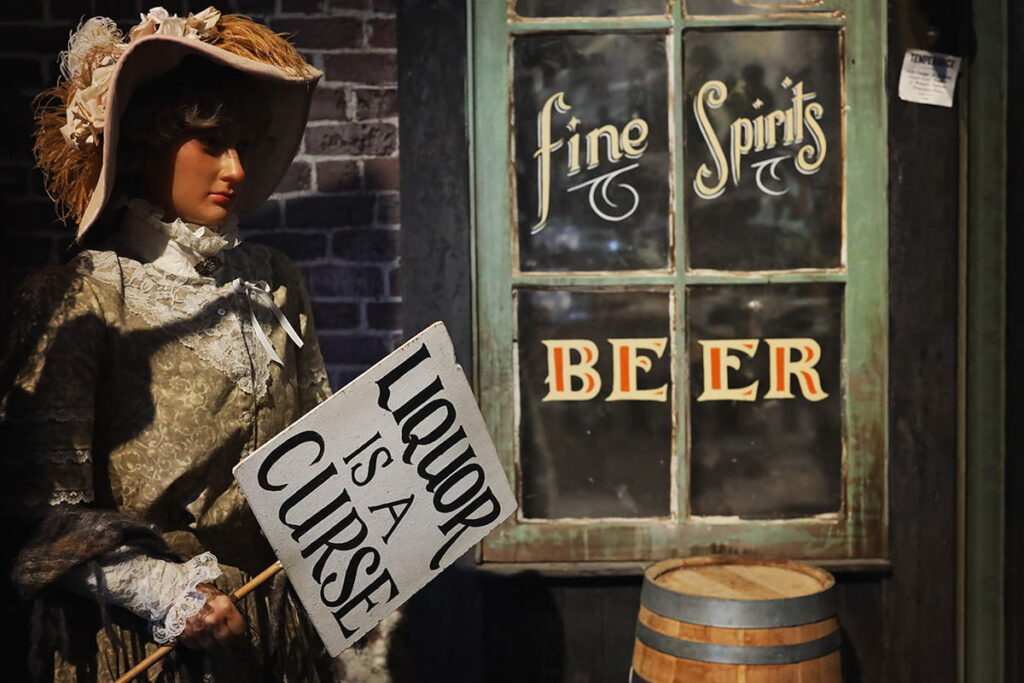 A still-life scene inside American Prohibition Museum shows the wax figure of a woman dressed in her Sunday best and standing in front of a saloon while holding a sign that reads "Liquor is a Curse"