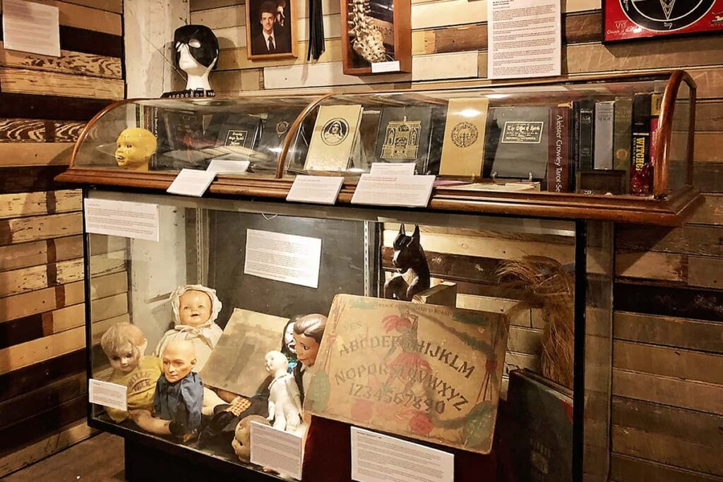 A glass display case in Graveface Museum features a frightening collection of dolls, Ouija boards, and books on witchcraft