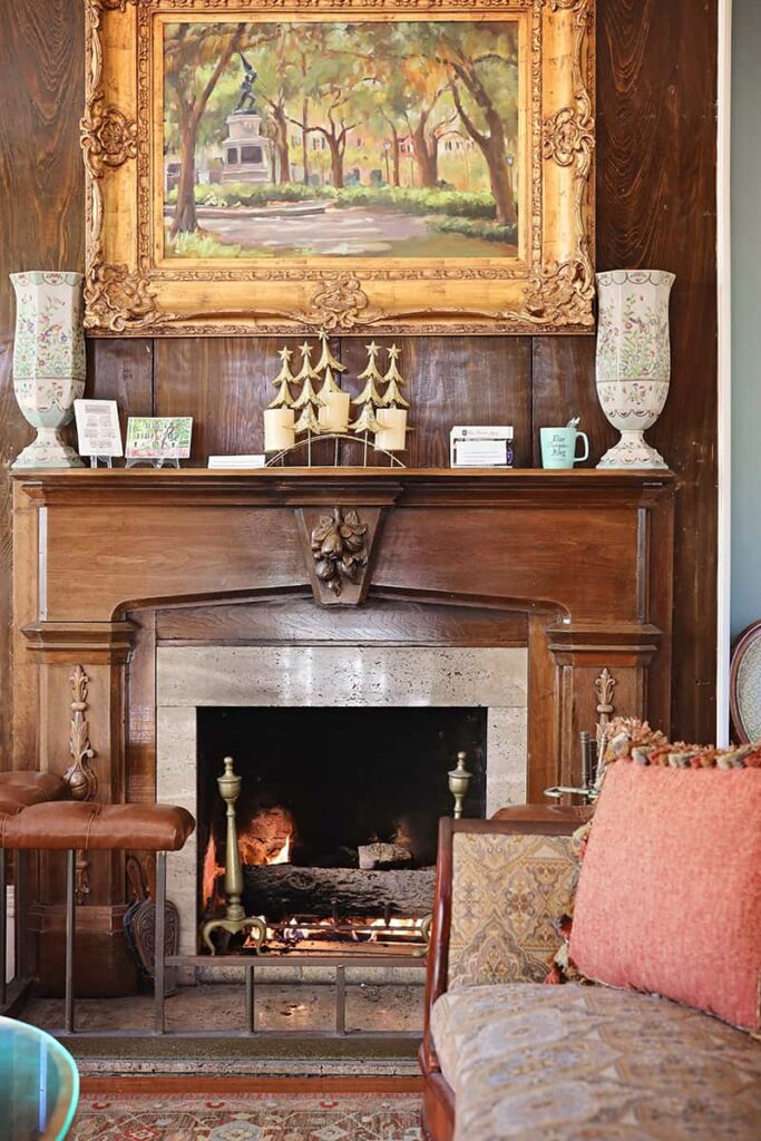 A cozy fireplace scene in the parlor of the Eliza Thompson House shows a painting of Savannah hanging in a gilded frame above a wooden mantle
