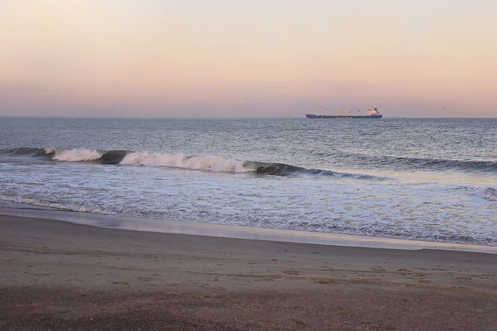 Tybee Island's North Beach with gentle 2-foot waves awash in a pale pink glow from the sunset and a cargo ship visible in the distance