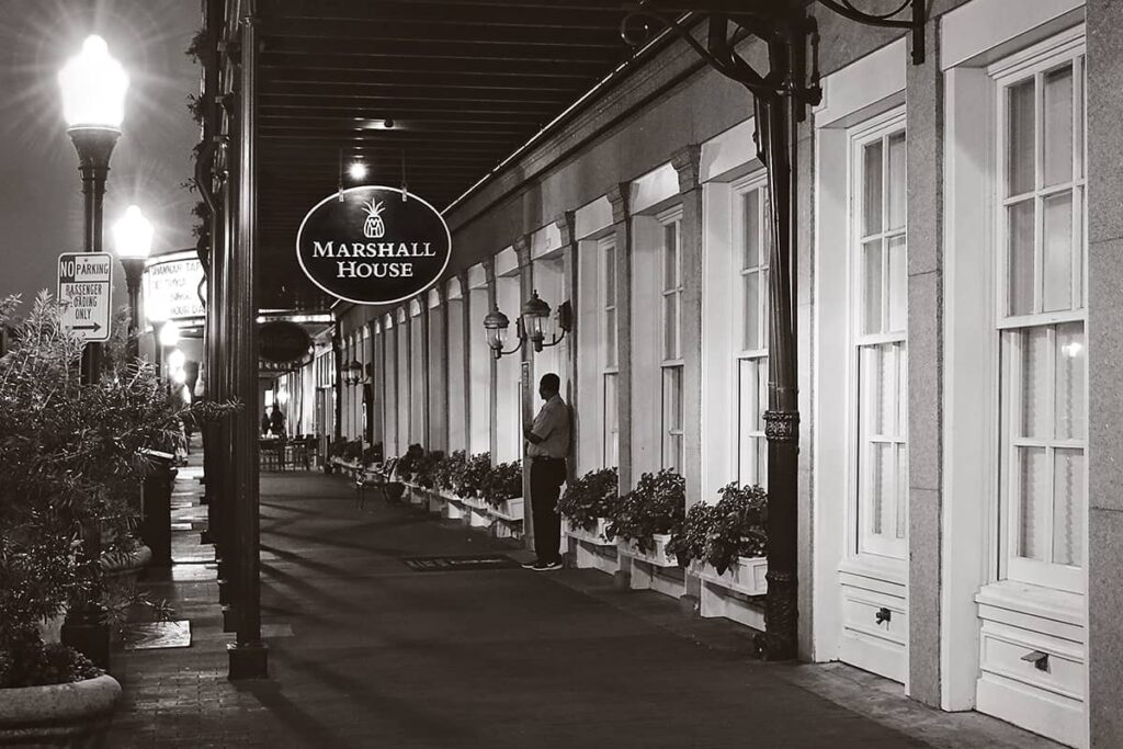 Front entrance to The Marshall House at night with a man standing beneath the hotel's sign, facing away from the camera