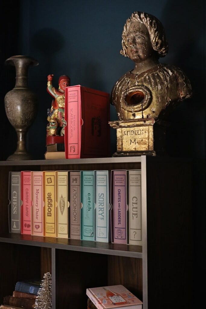 Bookshelf inside Perry Lane Hotel with a statue on the top shelf and popular board games arranged artfully on the second shelf. The wall in the background is painted a rich peacock blue shade