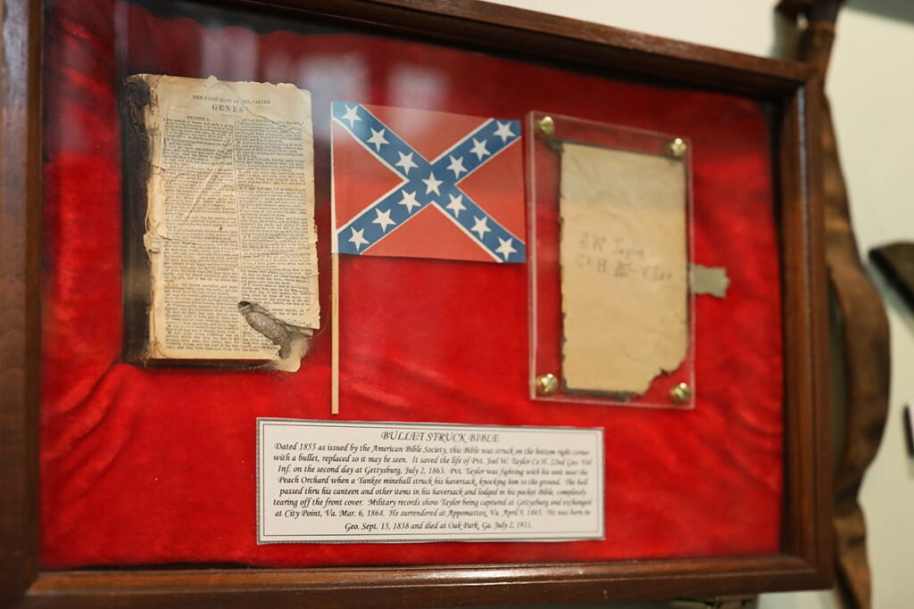 Wooden display case inside Webb Military Museum in Savannah with red velvet felt, a small Confederate flag, and a bible with a bullet lodged in its pages