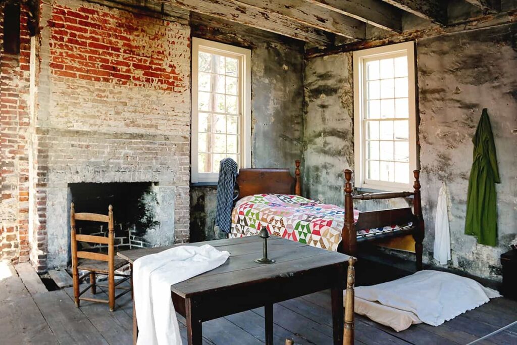 The quarters for enslaved families at the Owens-Thomas House shows simple wooden floors, exposed brick walls, and sparse furnishings
