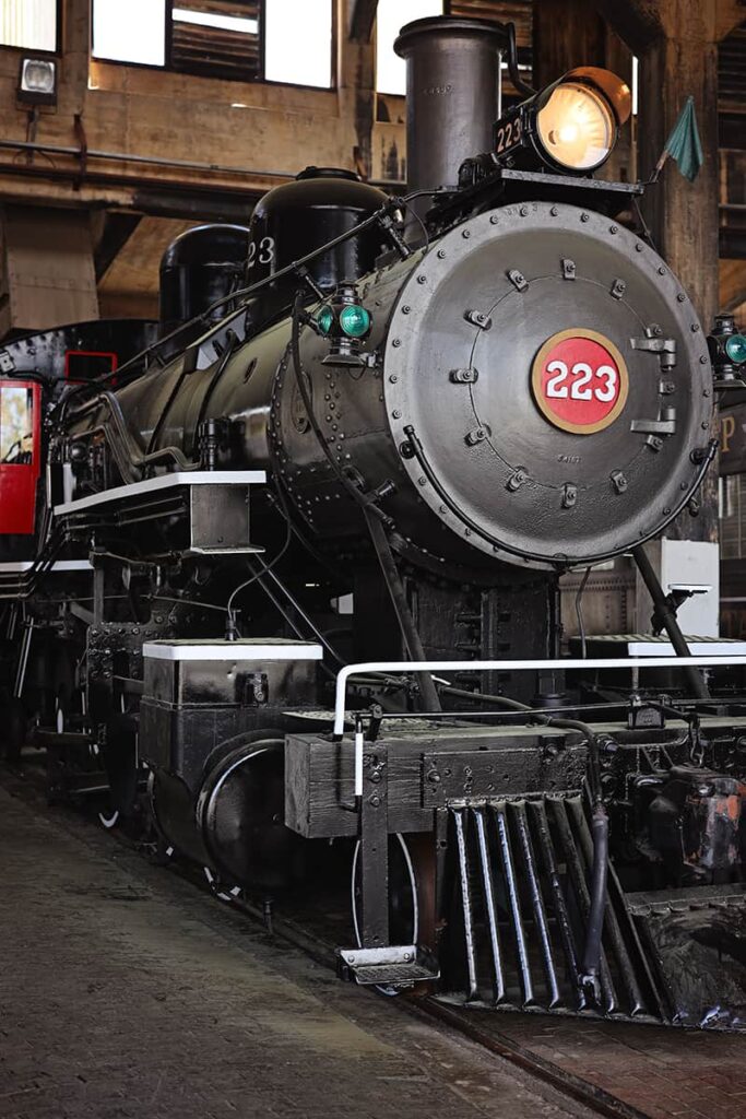 Front-facing shot of Engine #223 with its headlight glowing and the numbers 223 in white text against a red backdrop surrounded by a gold circle