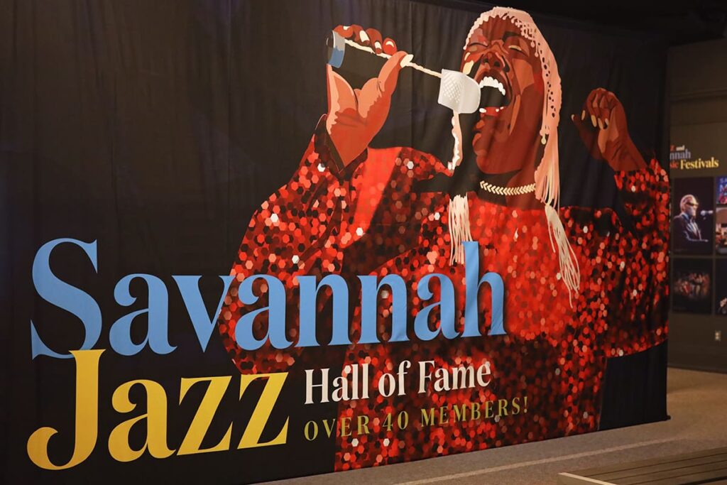 Oversized wall display showing a female jazz singer in a sparkly red dress with a microphone in her hand. The words "Savannah Jazz Hall of Fame" are layered atop the image