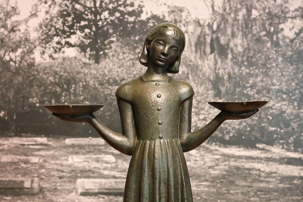 The famous bronze Bird Girl statue in front of a B&W background photo of Bonaventure Cemetery