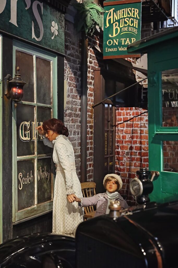 A scene inside American Prohibition Museum shows the wax figures of a woman and her young daughter peering into the window of a saloon with a sign indicating that the establishment has beer on tap