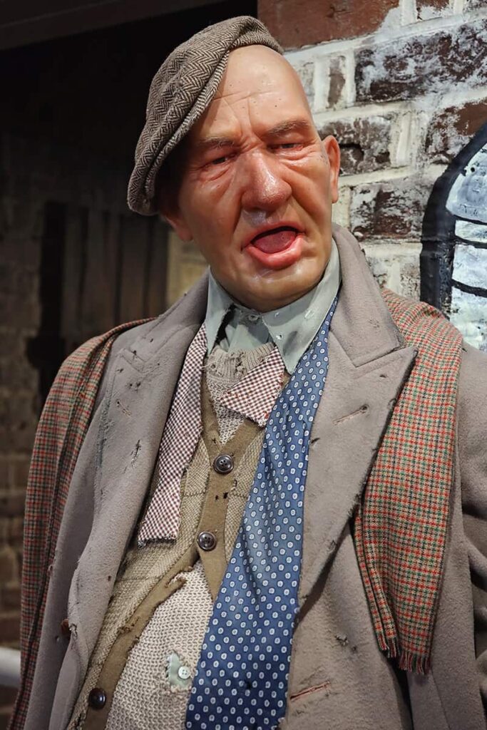 Wax figure of a drunkard inside American Prohibition Museum. His clothing is disheveled and torn, cap askew, and mouth hanging open in stupor
