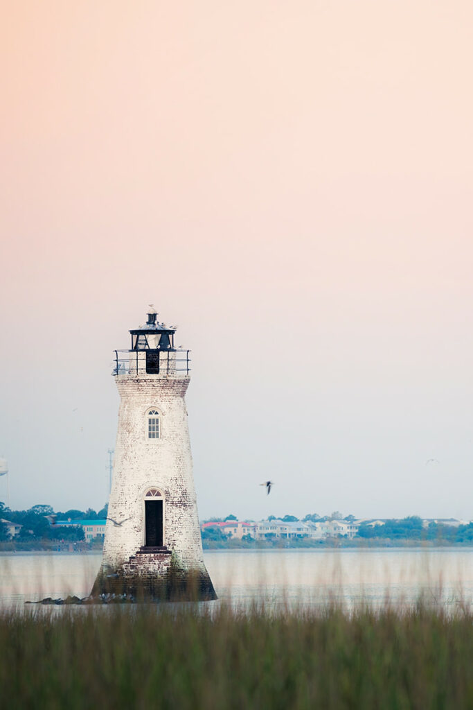A pale peach and blue sunset can be seen behind the white-painted brick Cockspur Lighthouse near Tybee Island