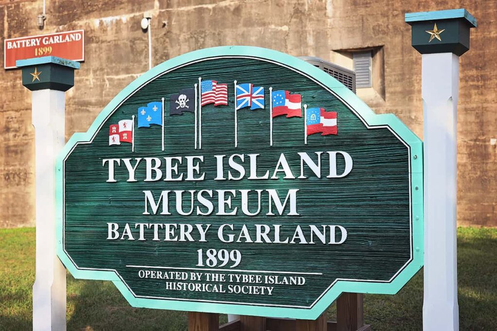 Green wooden sign with white lettering for the "Tybee Island Museum Battery Garland 1899 | Operated by the Tybee Island Historical Society"