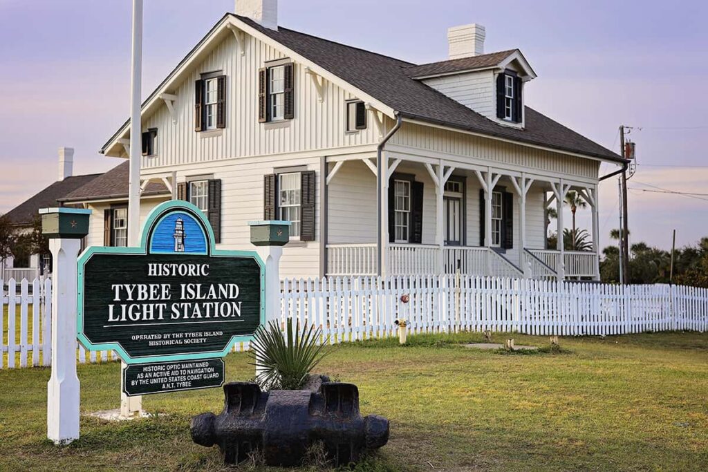 A small white cottage with a wooden sign in front of it indicating it's the site of the Historic Tybee Island Light Station