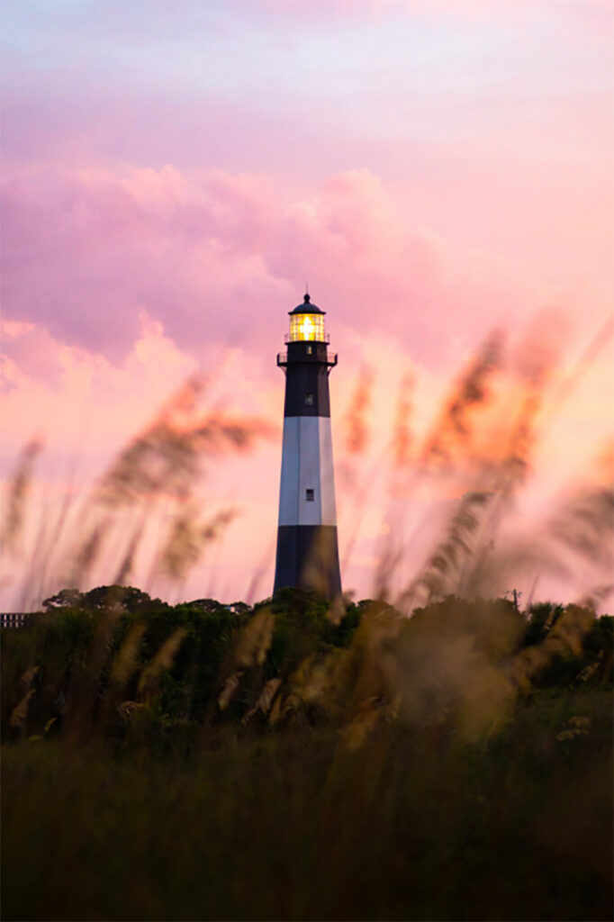 Peering through grassy beach dunes towards the Tybee Island lighthouse with a beautiful peach and pink sunset in the background