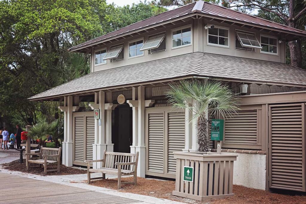 Two-story covered wooden building at Coligny Beach Park with bathrooms, changing stations, trash bins, benches, and an AED device