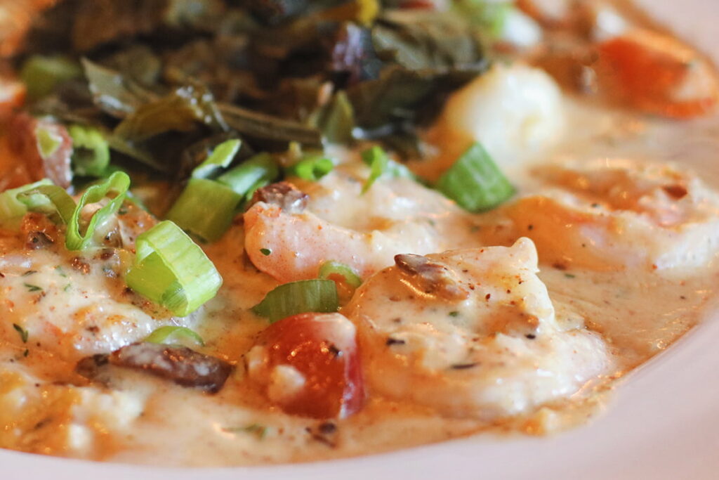 Bowl filled with shrimp and grits at B Matthews in Savannah. Seasoning is visible on the shrimp, and small tomatoes and green onions are mixed into the creamy sauce.