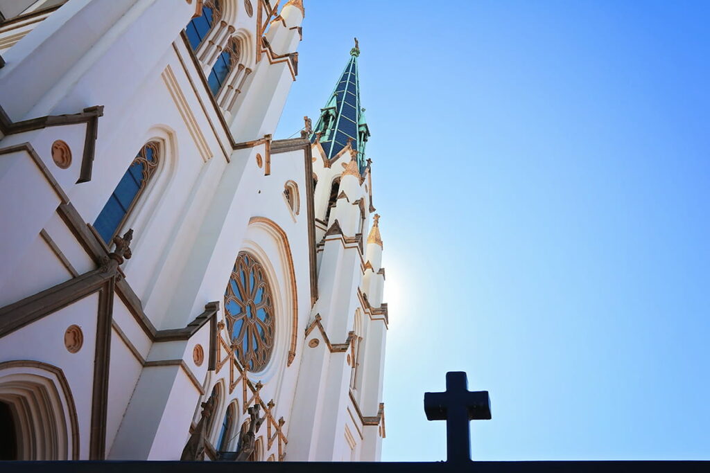 Exterior shot of the Cathedral Basilica of St. John the Baptist from a low angle with an iron cross from a fence prominent in the foreground