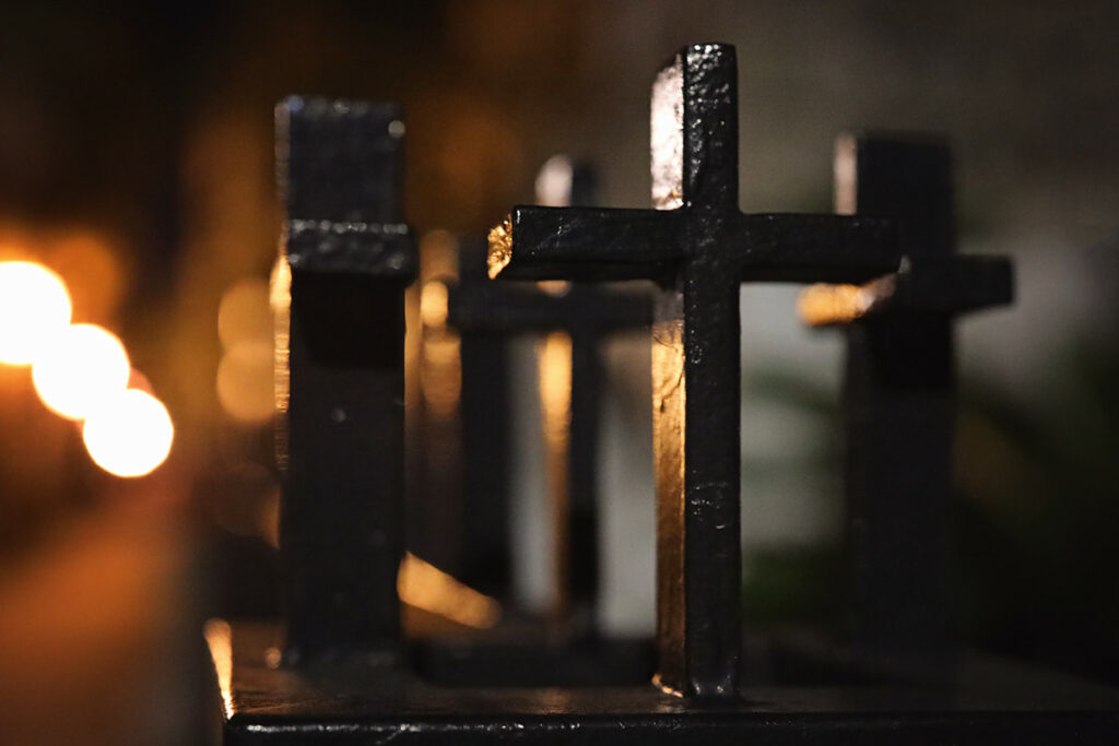 Black wrought-iron crosses atop a metal fence at Savannah's cathedral at night, illuminated by a dim streetlamp in the distance