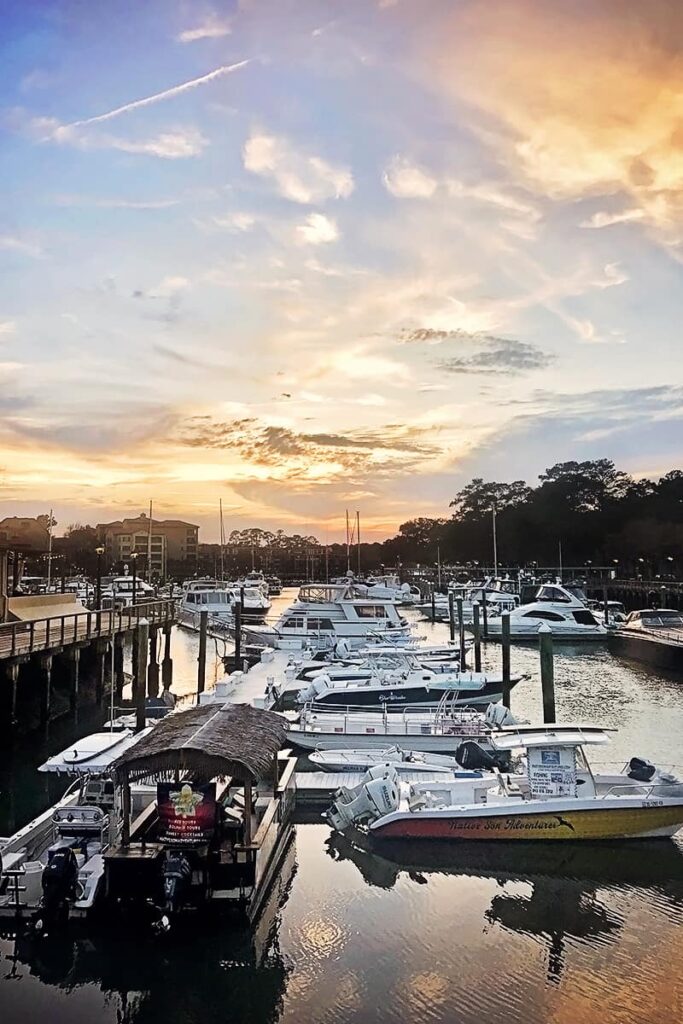 Dozens of luxury boats docked in Hilton Head's Shelter Cove Marina as the sun sets in shades of orange and yellow over the water