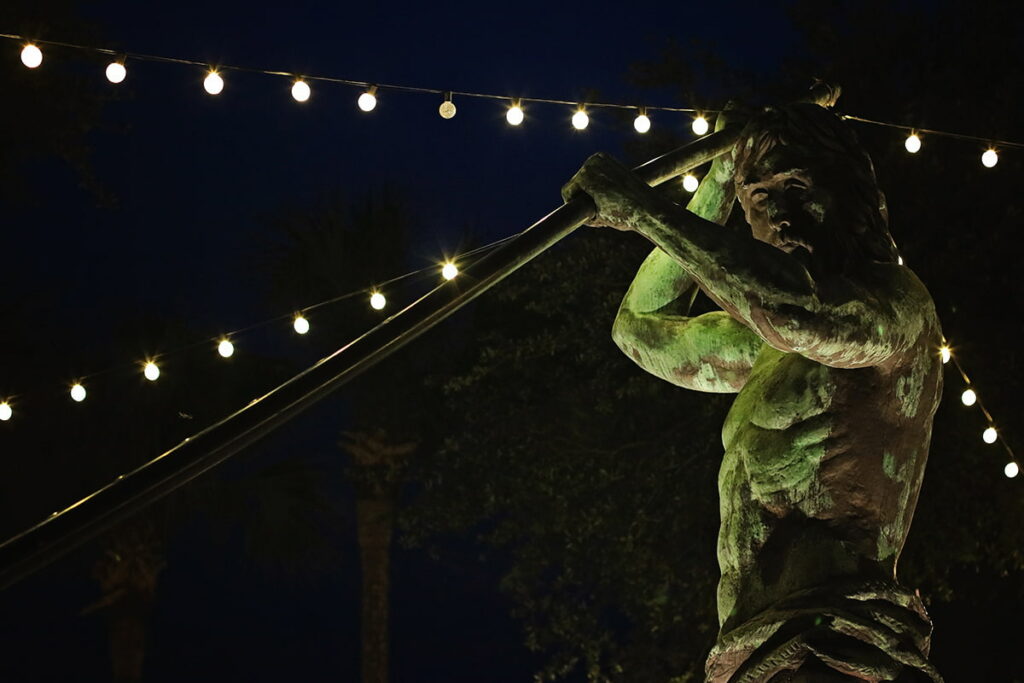 Nightime shot of the King Neptune statue in Shelter Cove Marina with twinkle lights illuminating the area
