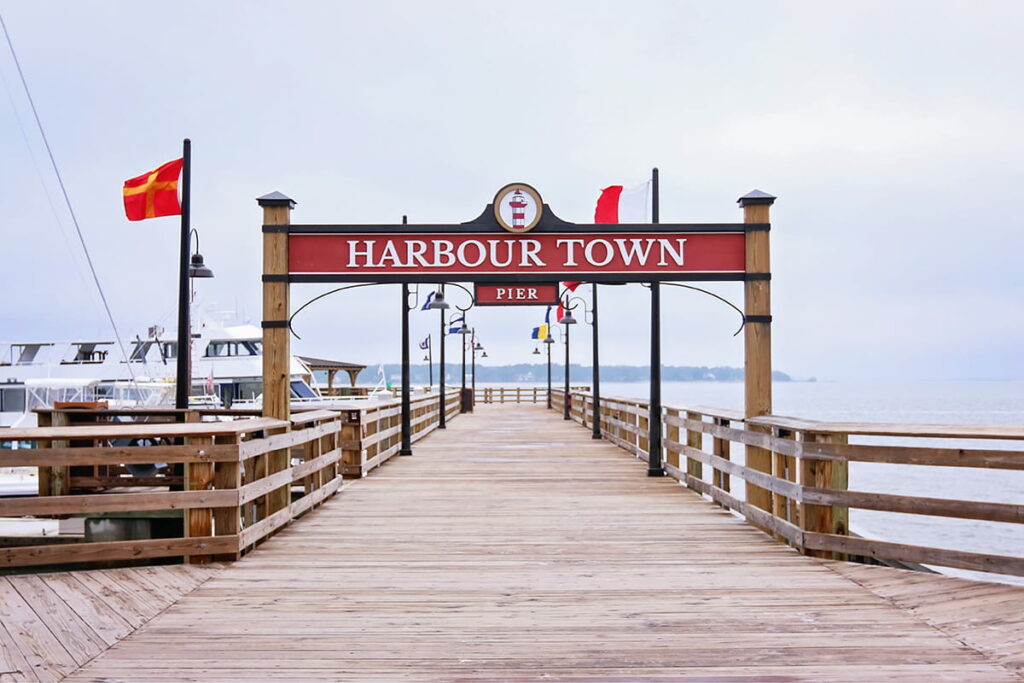 The red and white sign over the Harbour Town Pier is surrounded by colorful flags with yachts visible in the background