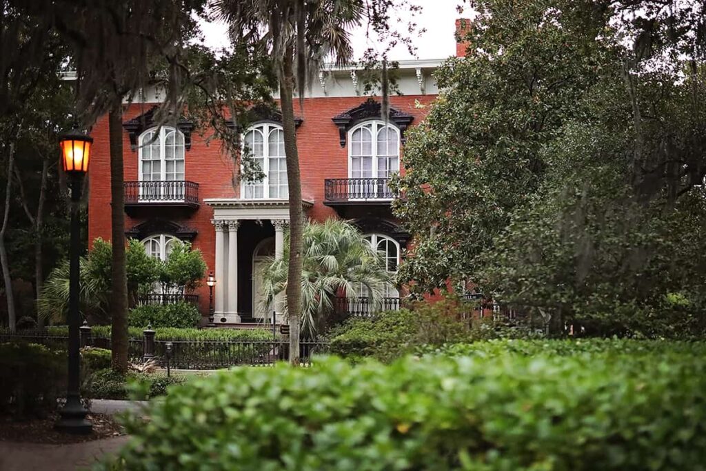 Looking through greenery in Monterey Square towards the red-brick façade of the Mercer Williams House, which is considered one of the most haunted houses in Savannah