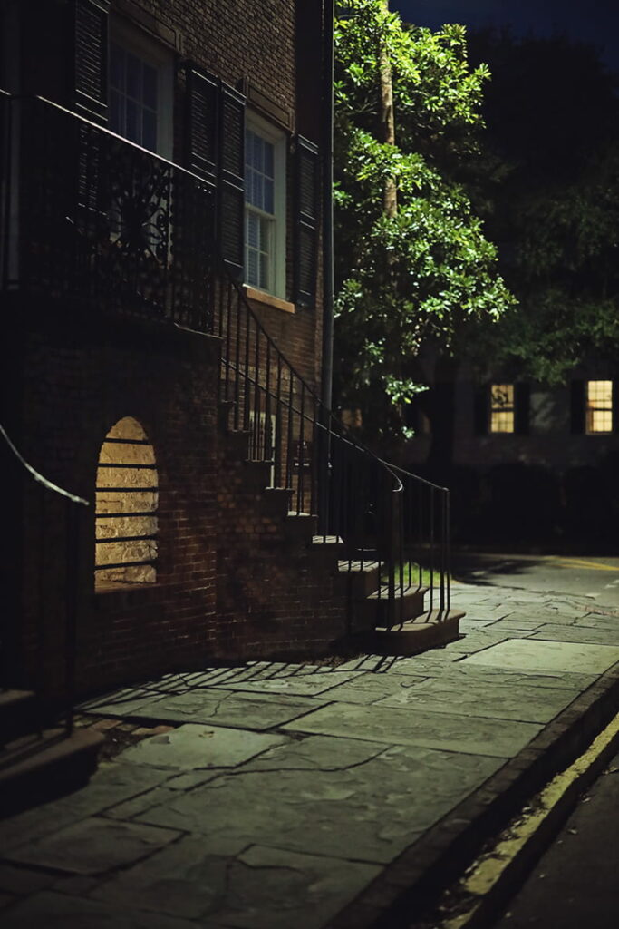 The façade of the Davenport House in Savannah looks spooky at night, with a pale yellow glow emanating from a barred vault located between the home's curved front staircases