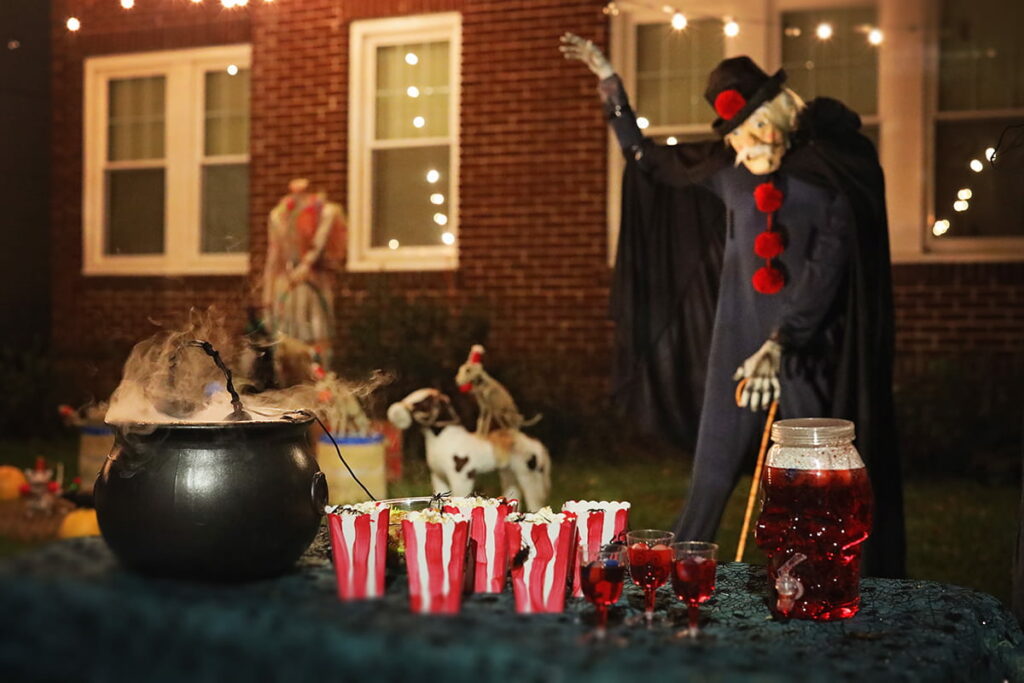 A ringmaster holds his skeletal hand up as if commanding his creepy crew to scare the neighborhood children. A black cauldron with smoke from dry ice sits on a table in the foreground