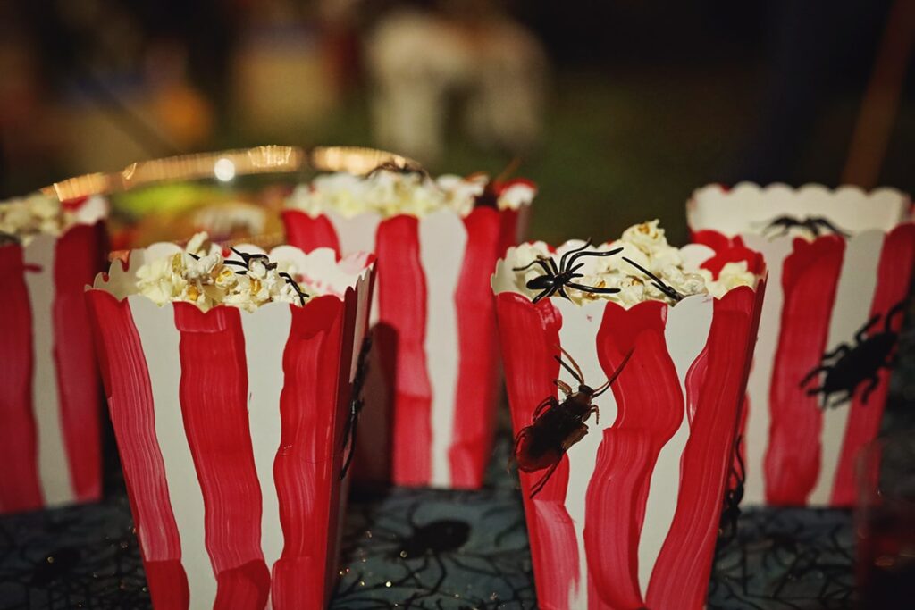 Roaches crawl across red and white striped popcorn containers atop a spidery tablecloth