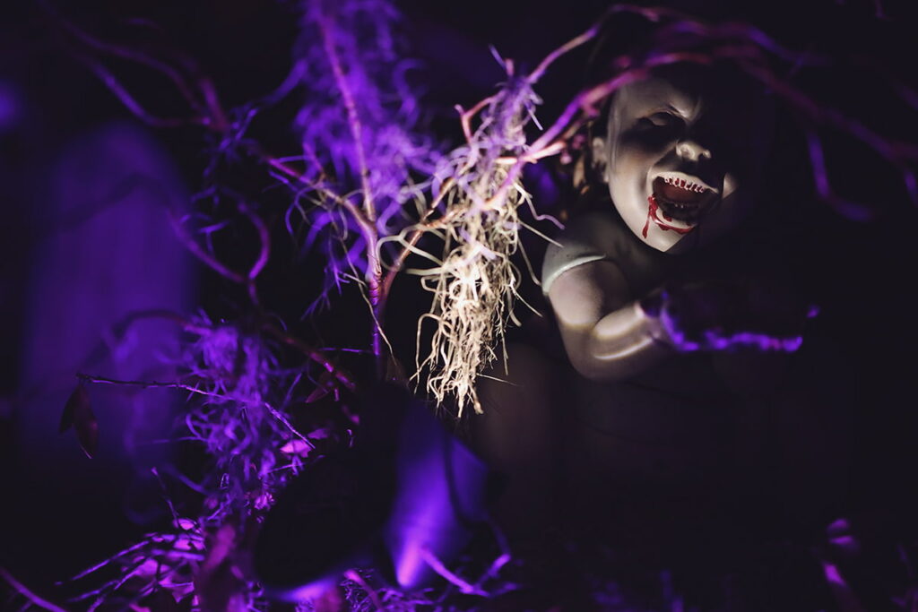 Spooky purple lights illuminate a doll surrounded by dead branches and Spanish moss
