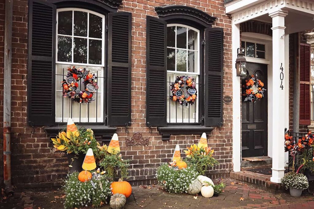 A beautiful home in Savannah decorated for Halloween with wreaths on the front door and two windows, plus wooden candy corn stakes sticking out of the fall planters beneath the windows