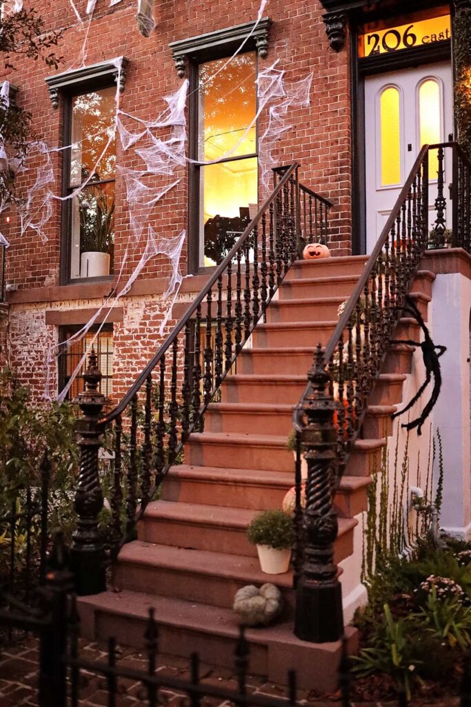 Elegant row house decorated for Halloween in Savannah, GA, with spiderwebs covering the bricks and giant spiders climbing the stairs