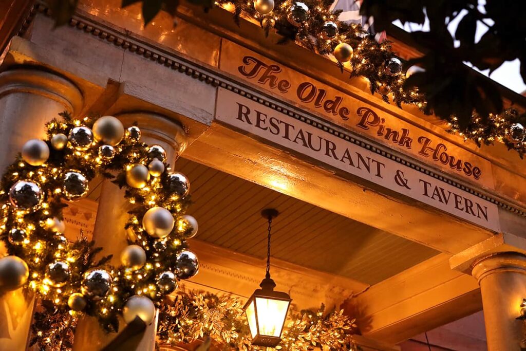 Close-up of a wooden sign with lettering indicating the entrance to "The Olde Pink House Restaurant & Tavern". A wreath and garlands surround the entrance